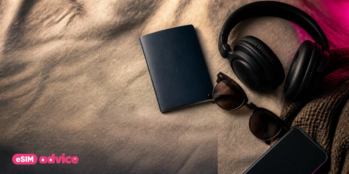 A flat-lay of a passport, sunglasses, headphones and a phone on linen