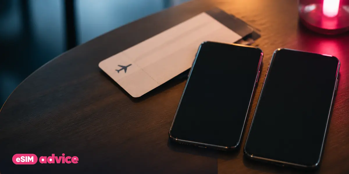 Two phones face-down side by side on a wooden table beside a boarding pass