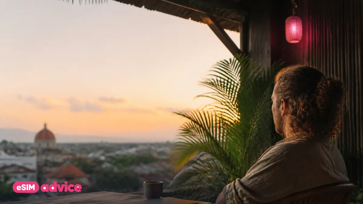 A nomad working from a sunlit balcony above a tropical city at golden hour