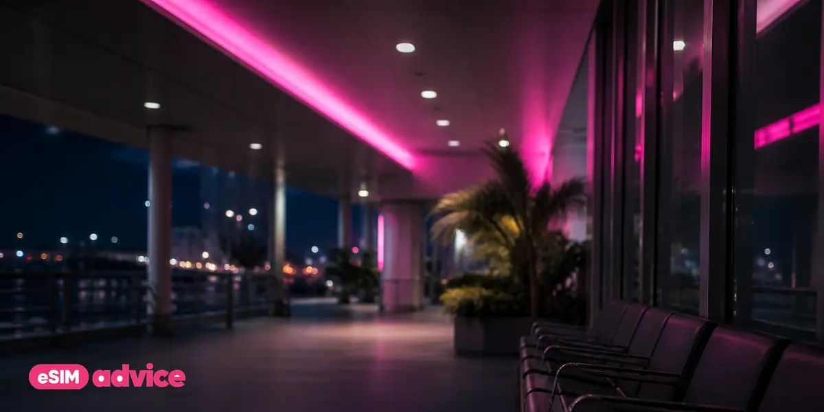 An arrivals corridor at night lit by a magenta ceiling strip