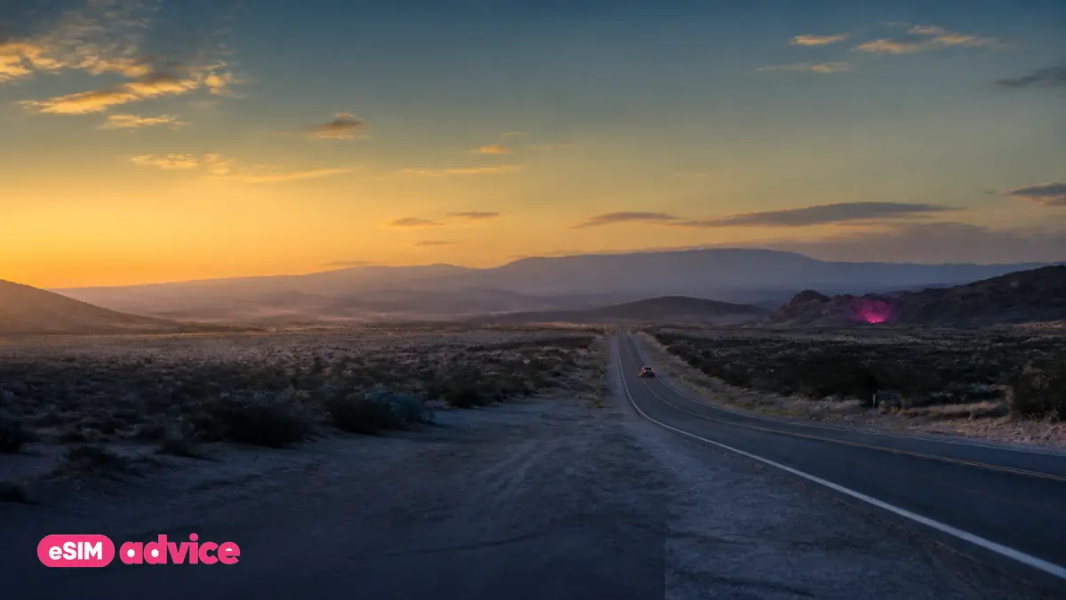 A wide desert highway at golden hour with a single distant car