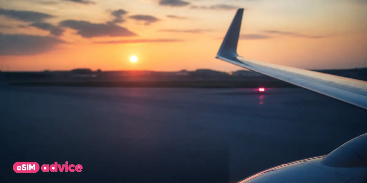 An aircraft window seat view of a runway at sunrise